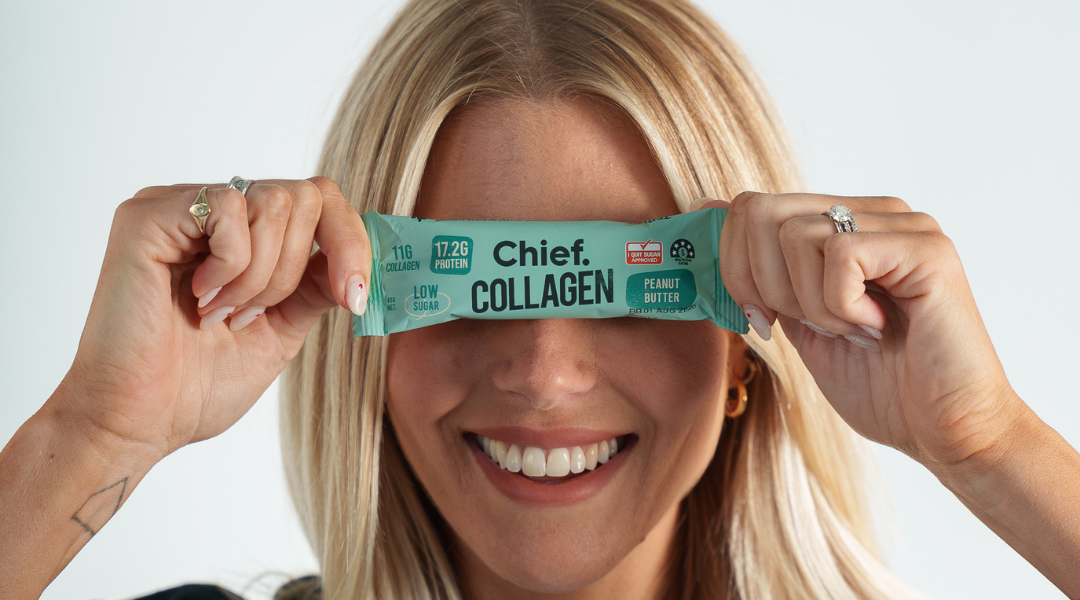 A woman's hands turning a protein bar over to read the ingredients panel on the back, in a warm home kitchen